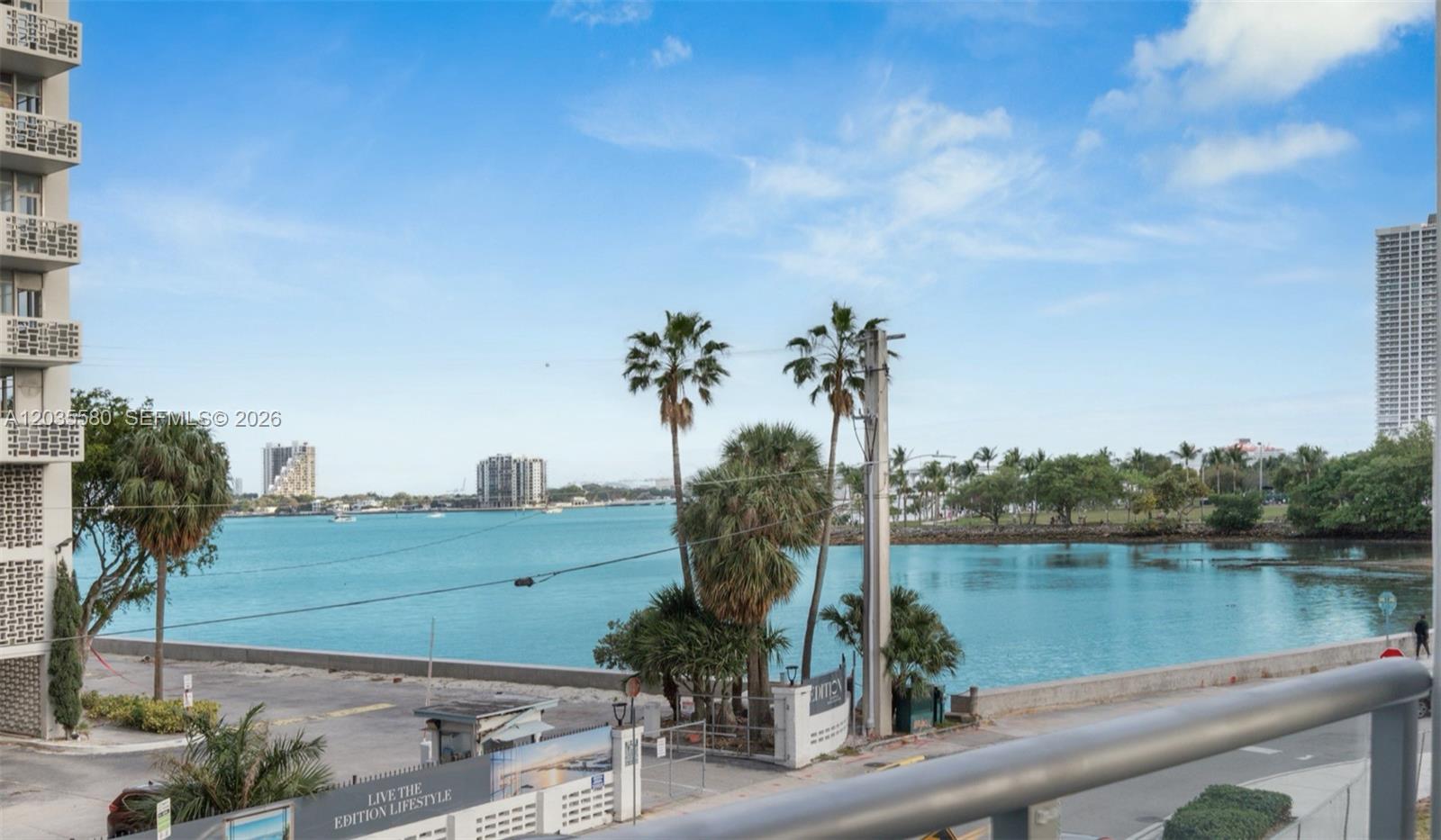 An elevated view of a bay with palm trees, a seawall, and distant buildings — MIAMI, FL