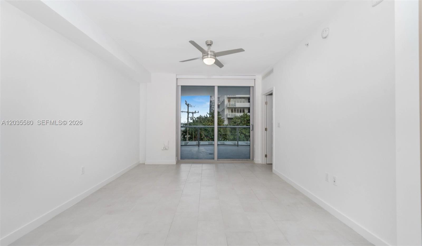An empty room with white walls, light tile flooring, a ceiling fan, and sliding doors — MIAMI, FL