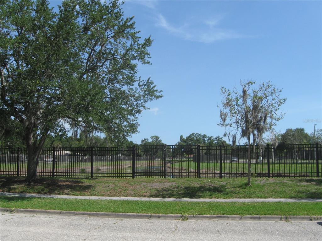 A black metal fence encloses a grassy lot with trees and a small pond — 1669 35TH STREET, SARASOTA, FL