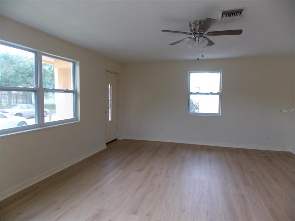 An empty living room features light wood-look flooring, cream walls, a ceiling fan, and windows — 1669 35TH STREET, SARASOTA, FL