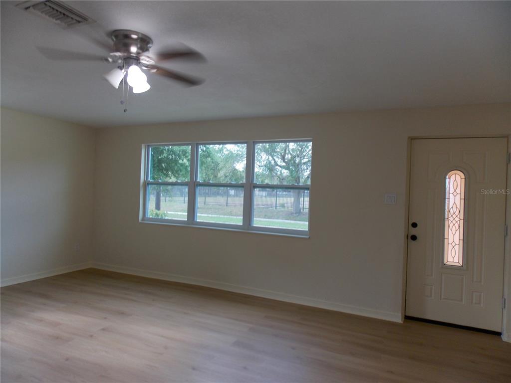 A living room features light wood-look flooring, a ceiling fan, and a front entry door — 1669 35TH STREET, SARASOTA, FL