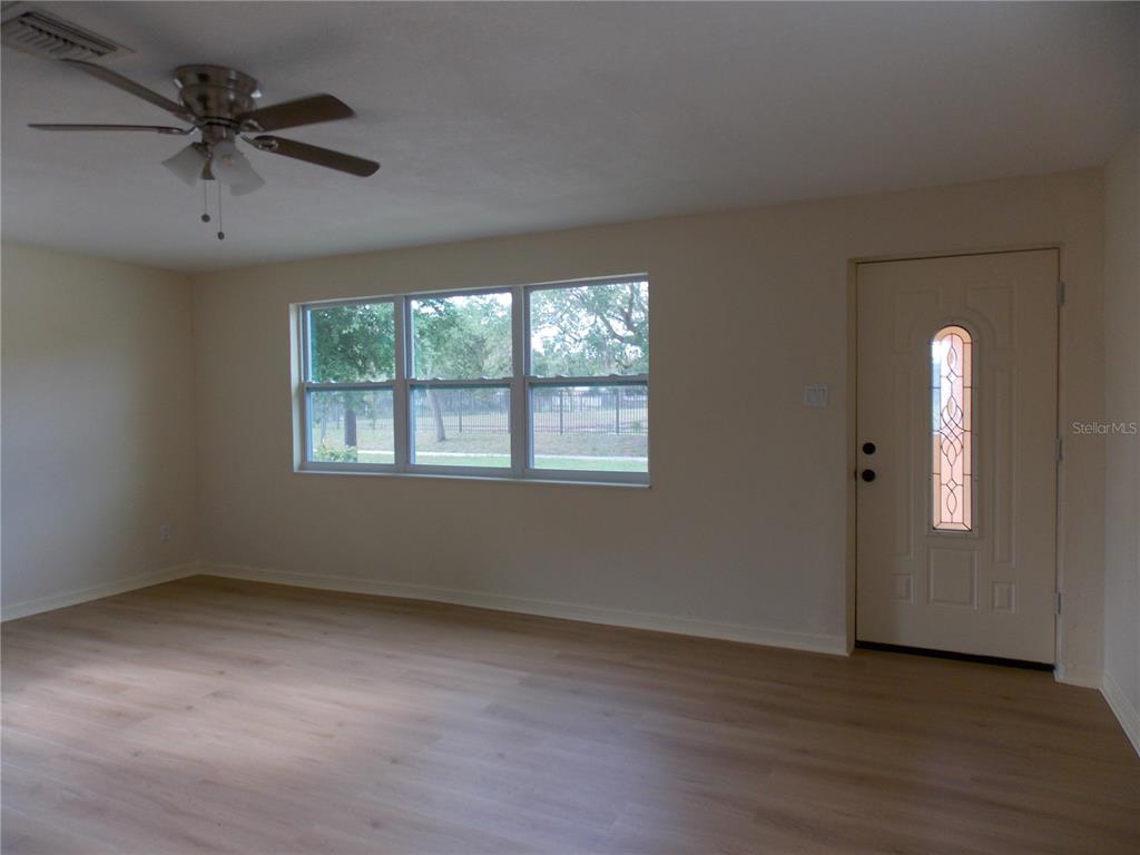 A living room with light wood-look flooring, a ceiling fan, and a front entry door — 1669 35TH STREET, SARASOTA, FL