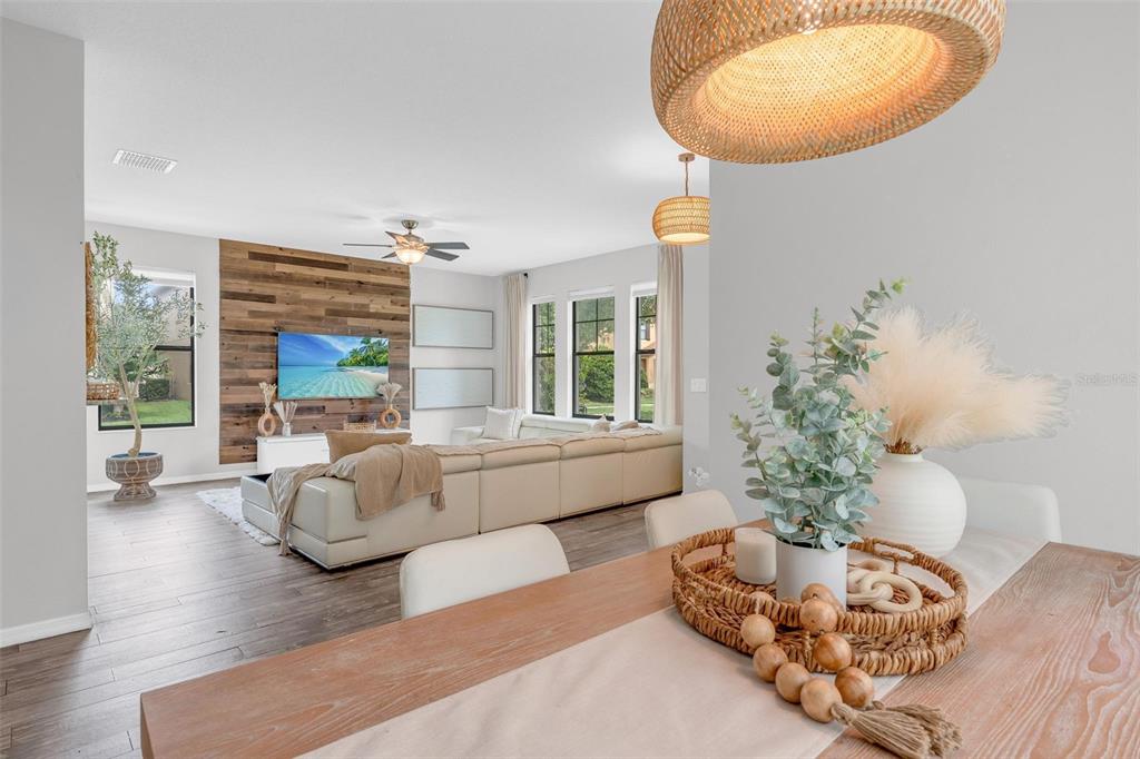 A dining area in the foreground overlooks a living room with a wood-paneled accent wall — 325 PARTRIDGE PEA LANE, OCOEE, FL