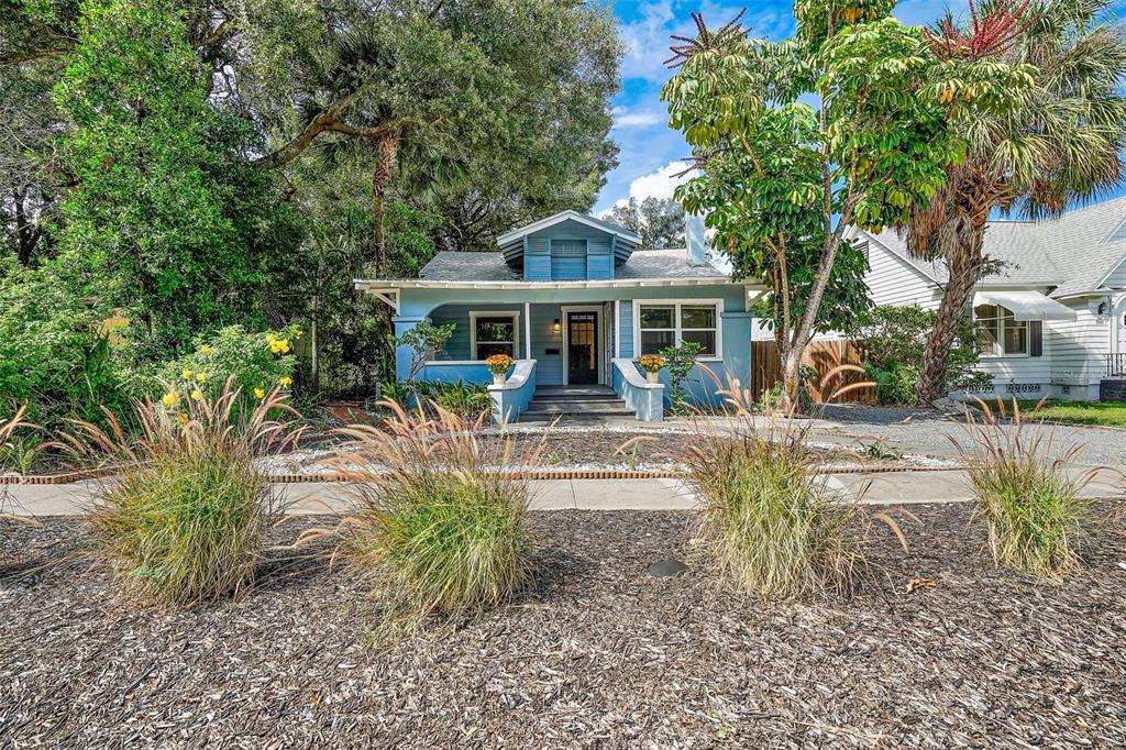A blue, single-story bungalow with a front porch sits behind a mulched yard with grasses — 2111 BURLINGTON AVENUE N, ST PETERSBURG, FL