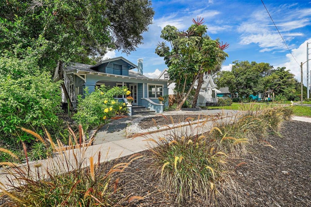 A blue bungalow with a front porch and landscaping sits behind a sidewalk and mulch — 2111 BURLINGTON AVENUE N, ST PETERSBURG, FL