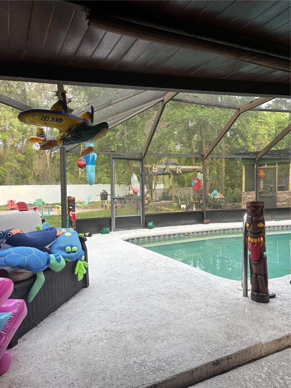 A screened-in pool patio features a tiki-themed bar, pool toys, and a wooden statue — 620 N SAVARY AVENUE, INVERNESS, FL