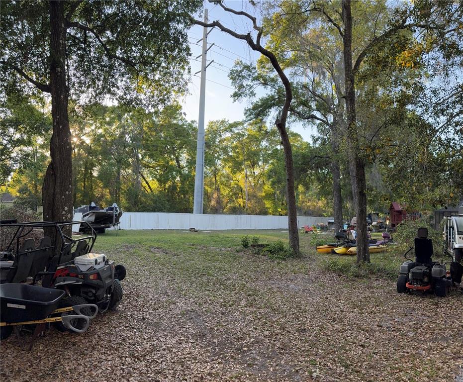 A grassy backyard features a white fence, mature trees, a utility pole, and various vehicles — 620 N SAVARY AVENUE, INVERNESS, FL