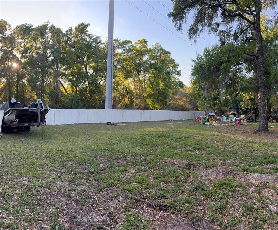 A grassy backyard features a boat on a trailer, a white fence, and patio furniture — 620 N SAVARY AVENUE, INVERNESS, FL