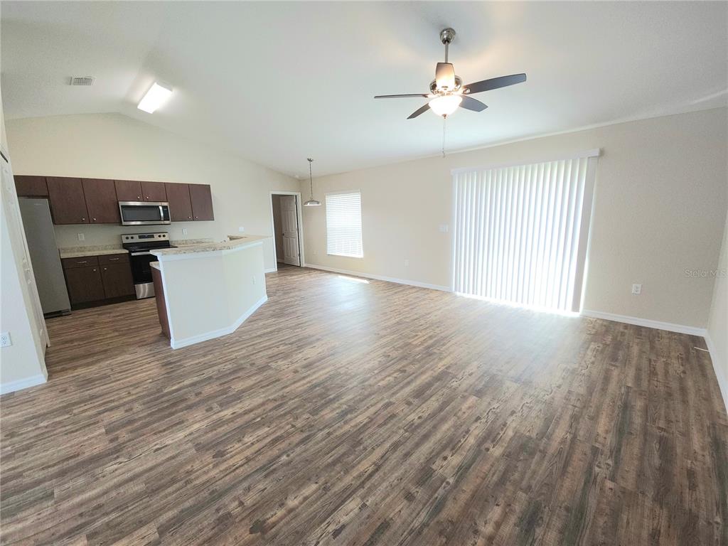 An open-concept kitchen and living area features wood-look flooring, a ceiling fan, and sliding doors — 13775 SW 43RD CIRCLE, OCALA, FL