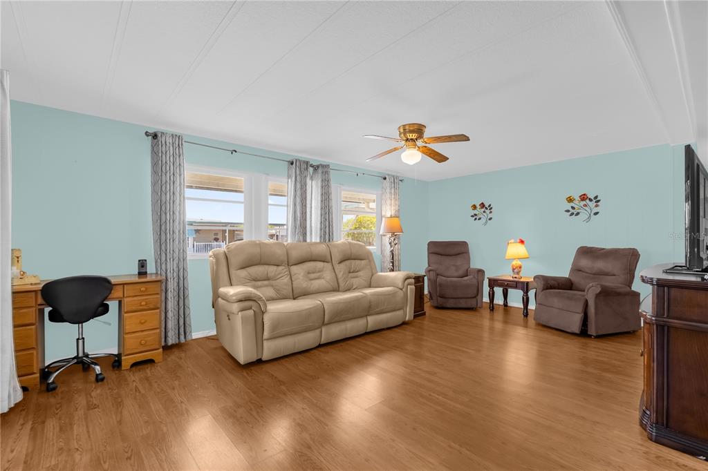 A living room with light blue walls, wood flooring, a beige sofa, and two recliners — 113 TROPICAL LANE, LEESBURG, FL