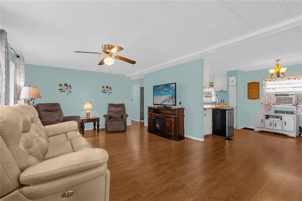 A living room with light blue walls, wood-look flooring, a ceiling fan, and a fireplace console — 113 TROPICAL LANE, LEESBURG, FL