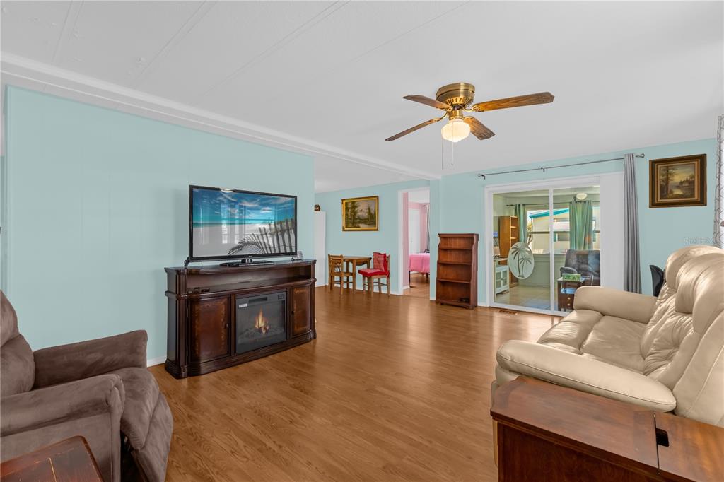 A living room with light blue walls, wood-look flooring, a ceiling fan, and a fireplace — 113 TROPICAL LANE, LEESBURG, FL