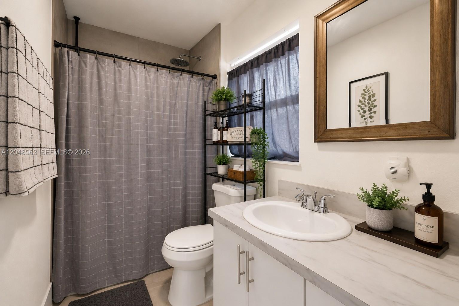 A bathroom features a white vanity, a toilet, a shower with a gray curtain, and a mirror — 14404 SW 105th Ct, Miami FL 33176, MIAMI, FL