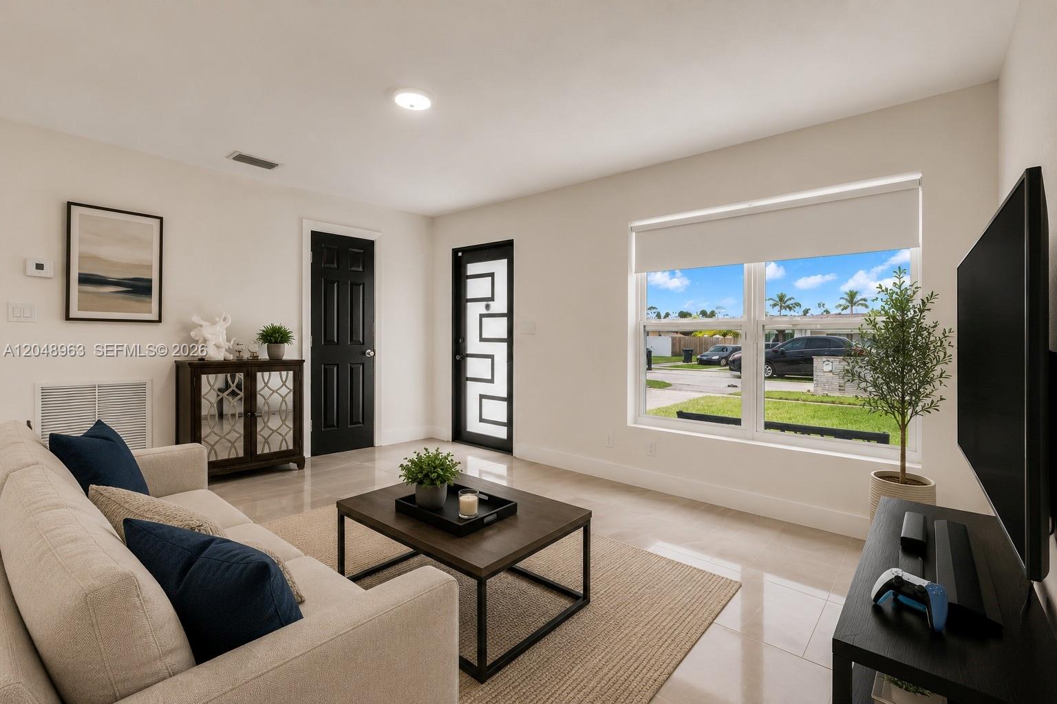 A living room features a beige sofa, coffee table, television, and a modern front door — 14404 SW 105th Ct, Miami FL 33176, MIAMI, FL