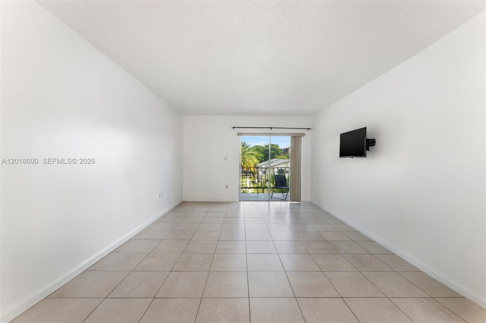 An empty living room features white walls, light-colored tile flooring, and a sliding glass door — 1900 W 54th St # 220, Hialeah FL 33012, HIALEAH, FL