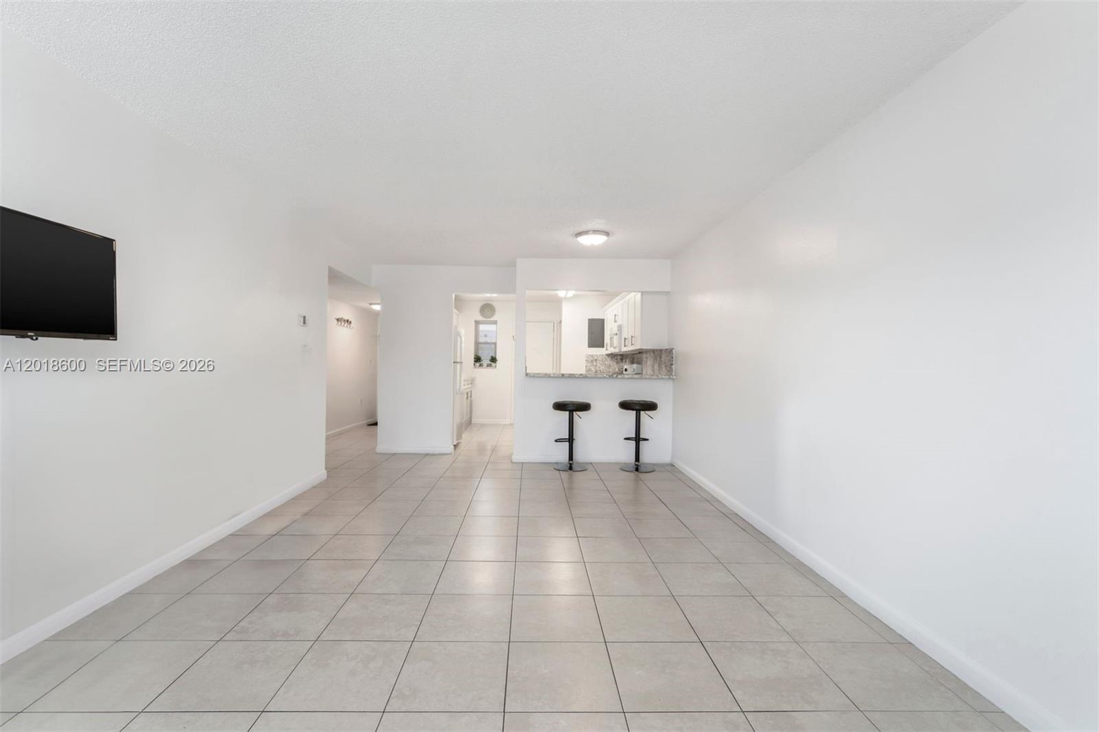 A living area with tile floors leads to a kitchen with a breakfast bar — 1900 W 54th St # 220, Hialeah FL 33012, HIALEAH, FL