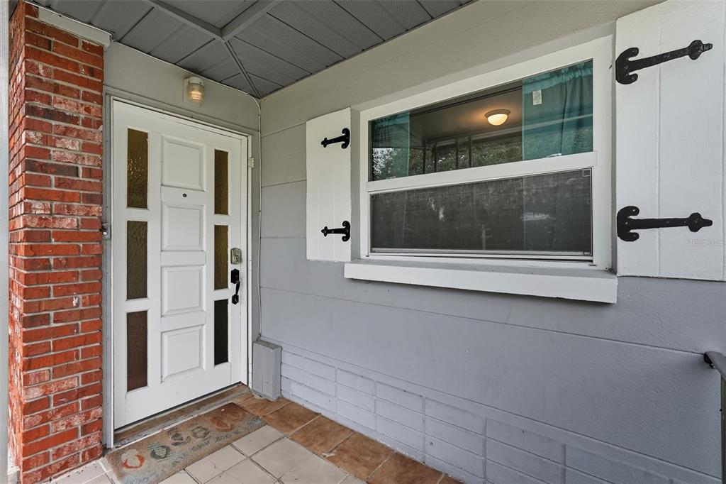 A front porch features a white door with glass panels, a window with shutters, and brick — 12361 114TH STREET, LARGO, FL
