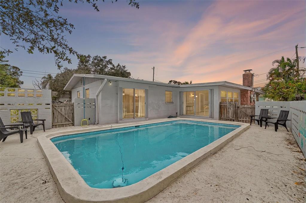 A backyard swimming pool sits in front of a single-story house with sliding glass doors — 12361 114TH STREET, LARGO, FL