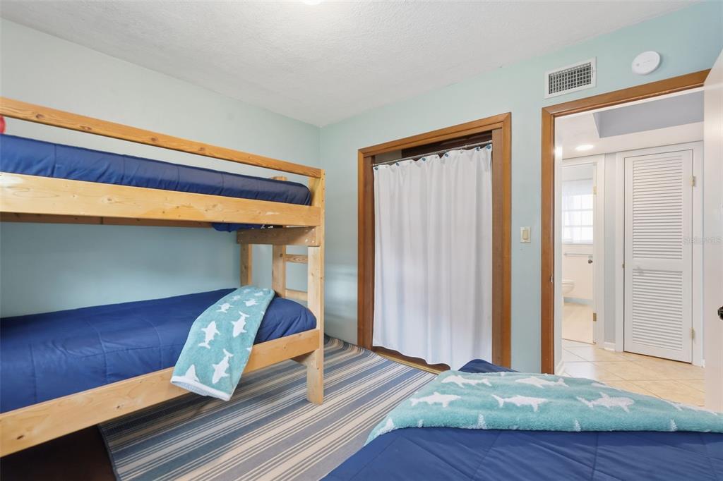 A bedroom features a wooden bunk bed, a single bed, and a doorway to a bathroom — 12361 114TH STREET, LARGO, FL