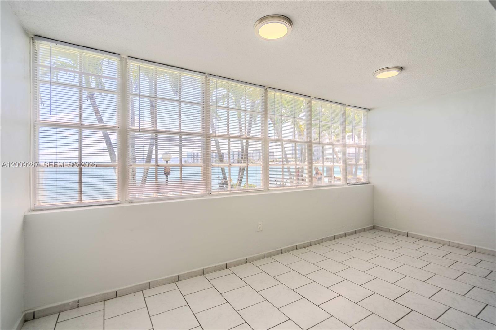 A sunroom with white tiled floors, two ceiling lights, and large windows overlooking palm trees — 1940 Bay Dr # 11, Miami Beach FL 33141, MIAMI BEACH, FL