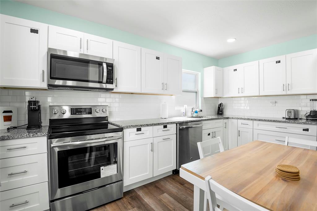 A kitchen features white cabinets, stainless steel appliances, granite countertops, and a wooden dining table — 1613 N MARTIN LUTHER KING JR AVENUE, CLEARWATER, FL