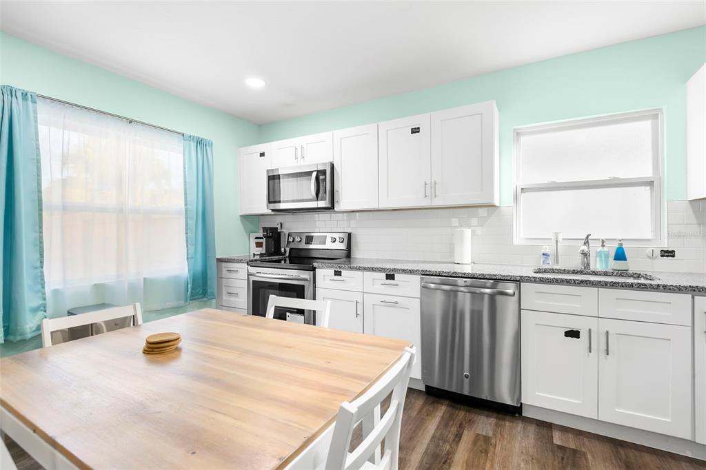 A kitchen with white cabinets, stainless steel appliances, granite countertops, and a wooden dining table — 1613 N MARTIN LUTHER KING JR AVENUE, CLEARWATER, FL