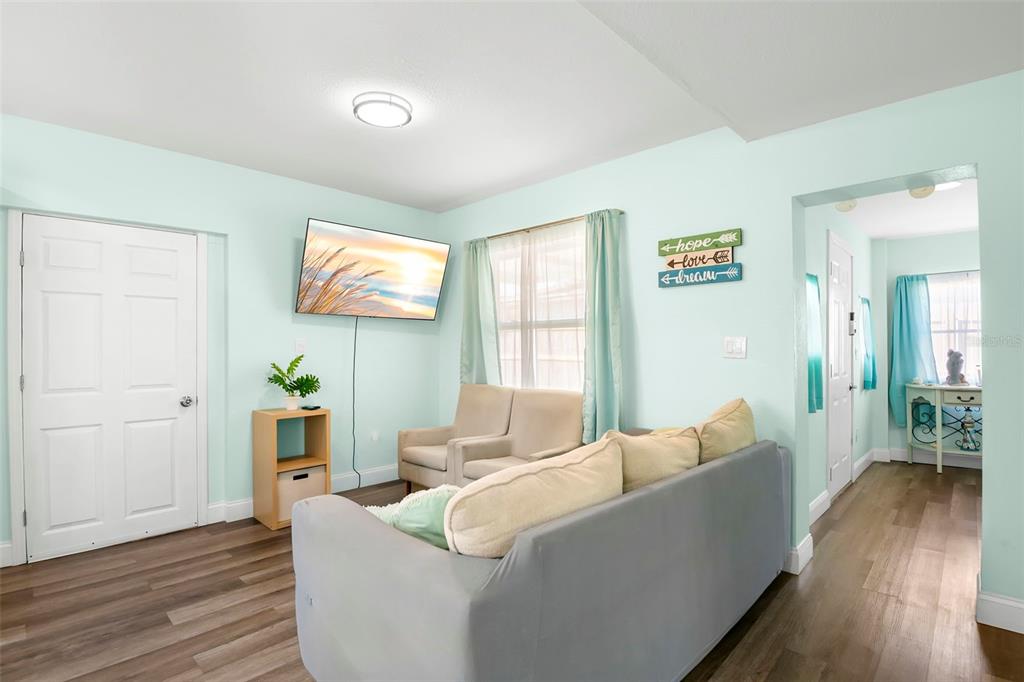 A living room features light blue walls, wood-look flooring, a sofa, and a wall-mounted television — 1613 N MARTIN LUTHER KING JR AVENUE, CLEARWATER, FL