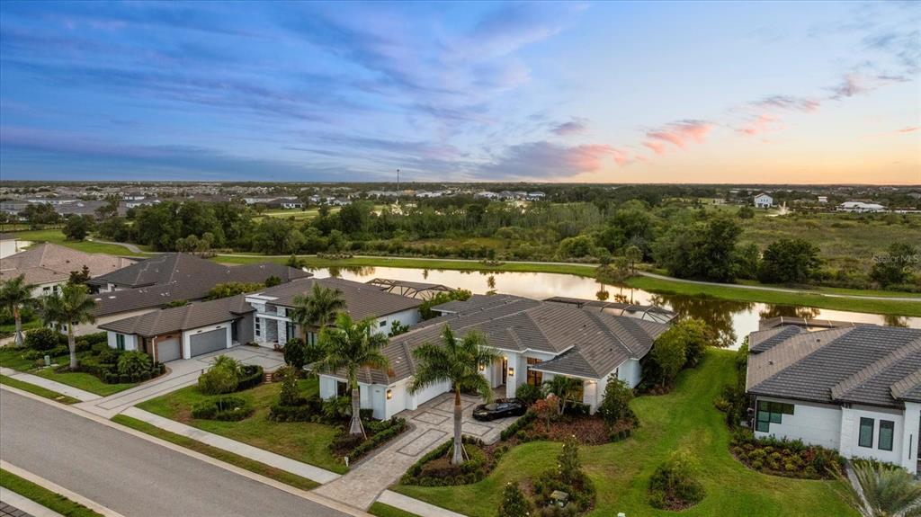 An aerial view of a suburban house with a paved driveway, palm trees, and pond — 4202 BUTTE TRAIL, BRADENTON, FL