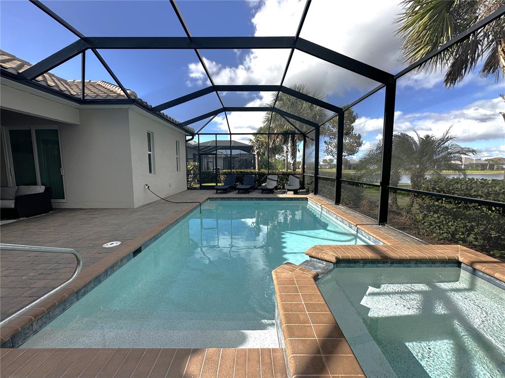 A screened-in pool and spa area with a paved deck and views of a lake — 25222 KEYGRASS COURT, PUNTA GORDA, FL