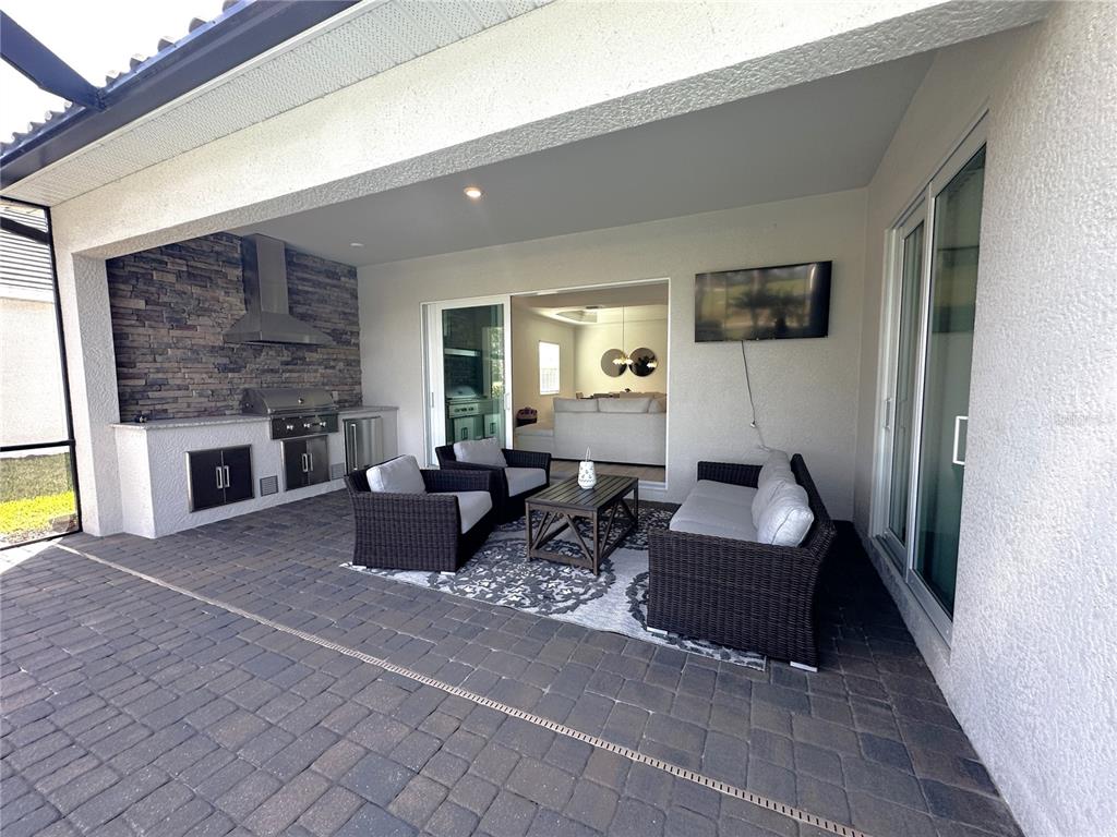 A covered patio features a stone-accented outdoor kitchen, seating area, and sliding glass doors — 25222 KEYGRASS COURT, PUNTA GORDA, FL