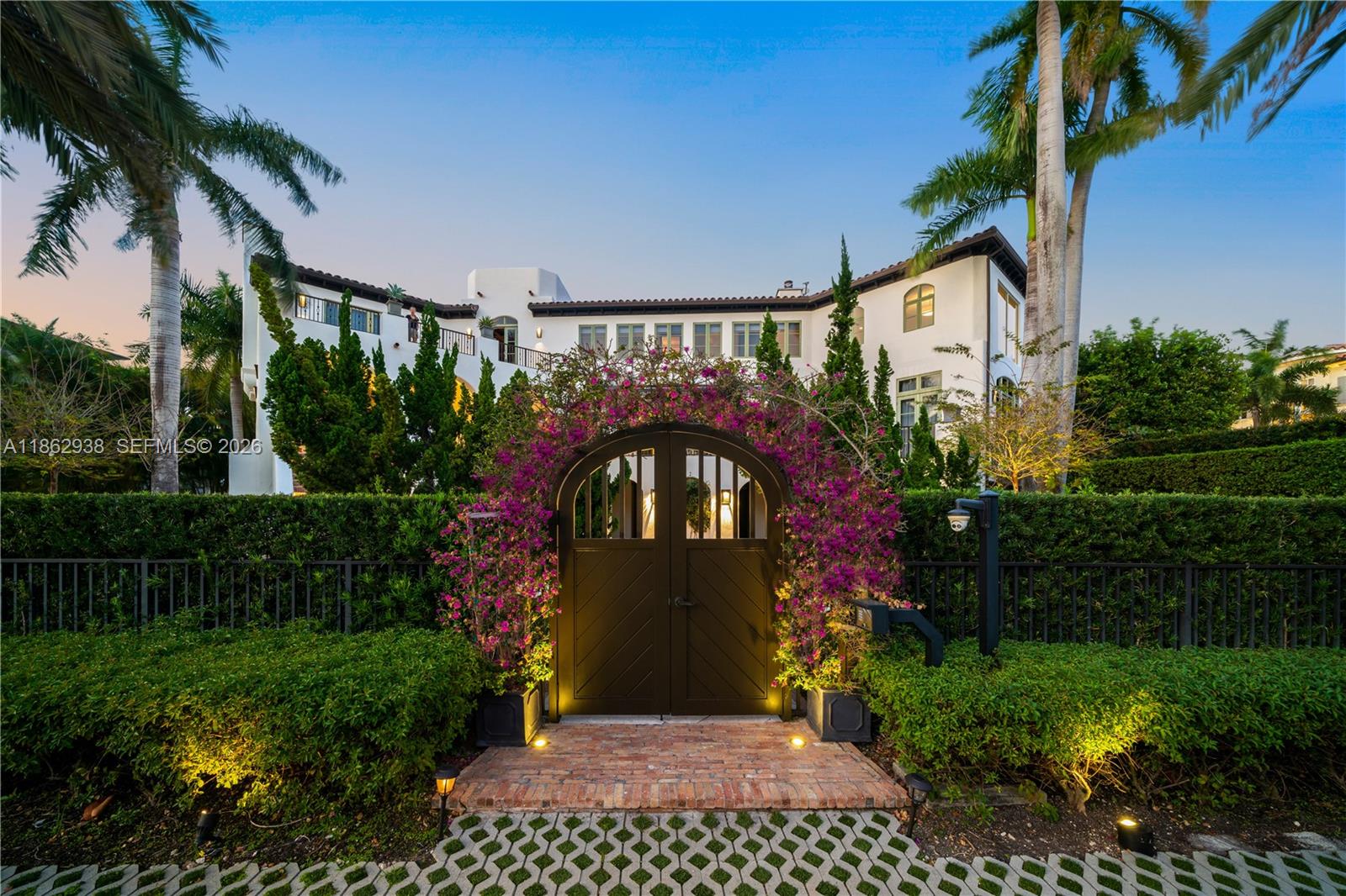 A white Mediterranean-style house features a gated entrance framed by blooming bougainvillea and palm trees — 3305 S Moorings Way, Miami FL 33133, MIAMI, FL