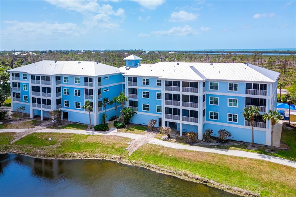 An aerial view of a three-story blue apartment building situated next to a pond — 8405 PLACIDA ROAD UNIT 206, PLACIDA, FL
