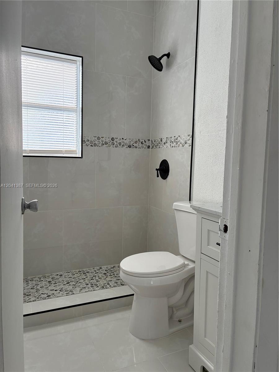A small bathroom features a walk-in shower with pebble flooring and a white toilet — 550 NW 15th Ct, Pompano Beach FL 33060, POMPANO BEACH, FL