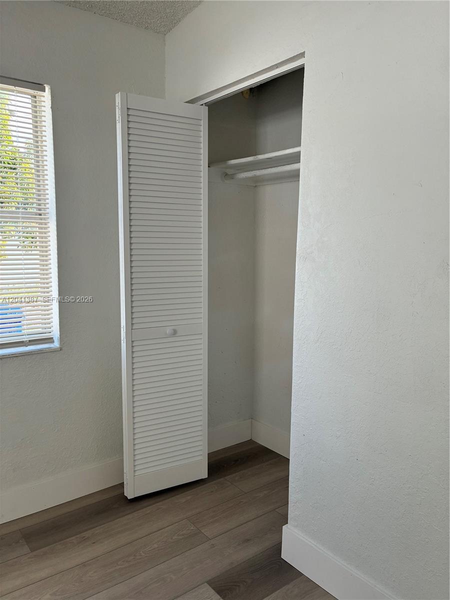 A room features white walls, wood-look flooring, a window with blinds, and an open closet — 550 NW 15th Ct, Pompano Beach FL 33060, POMPANO BEACH, FL