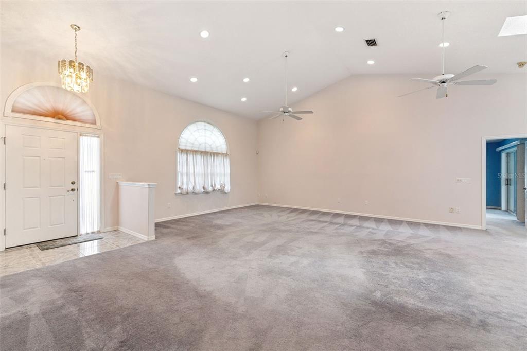 A spacious living room features vaulted ceilings, gray carpeting, two ceiling fans, and arched windows — 23 WELLSTREAM LANE, PALM COAST, FL