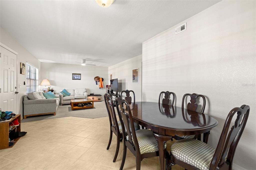 A dining area with a wooden table and chairs transitions into a carpeted living room — 6100 GULFPORT BOULEVARD S UNIT 414, GULFPORT, FL