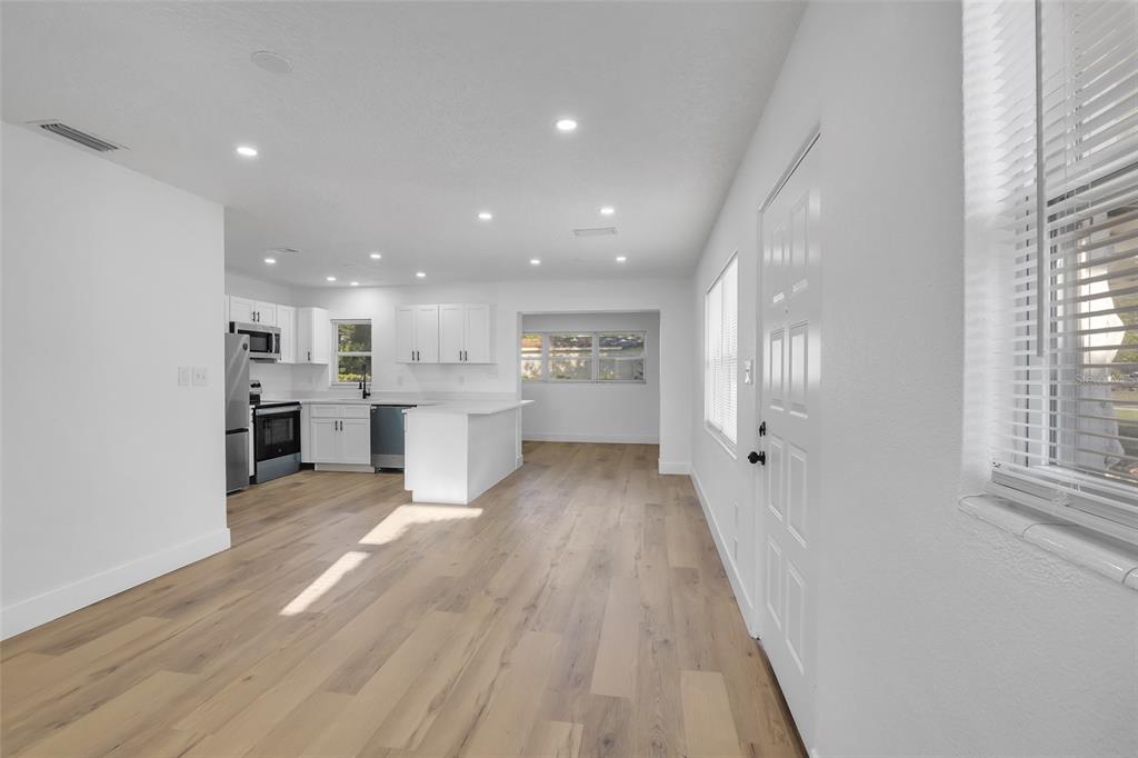 An open-concept kitchen and living area features white cabinetry, light wood flooring, and recessed lighting — 6108 BEAR LAKE TERRACE, APOPKA, FL