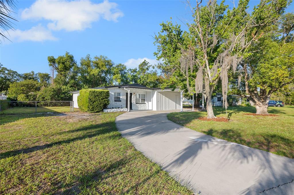 A white single-story house with a concrete driveway and a carport sits on a lawn — 6108 BEAR LAKE TERRACE, APOPKA, FL