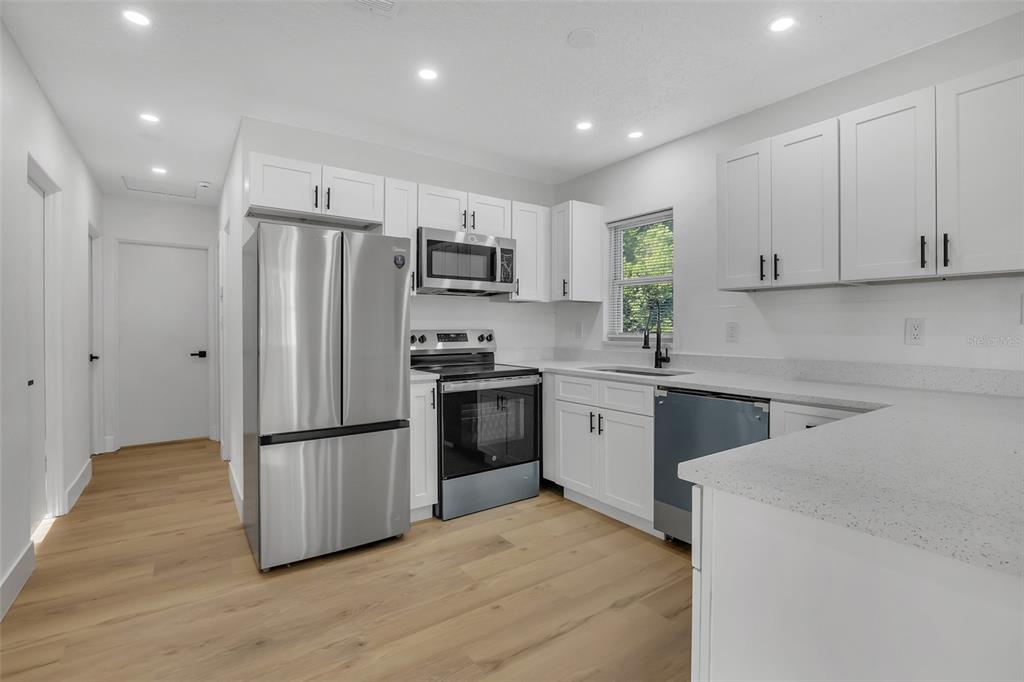 A modern kitchen features white cabinets, stainless steel appliances, and light wood-look flooring — 6108 BEAR LAKE TERRACE, APOPKA, FL