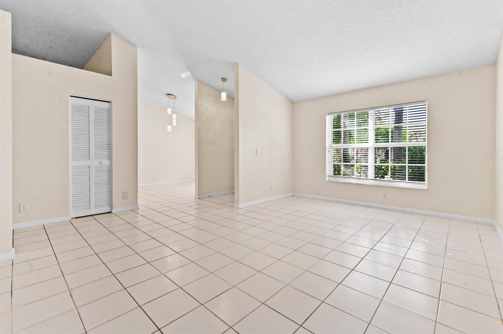 An empty room with light-colored tile flooring, beige walls, and a large window — 18377 Fresh Lake Way, Boca Raton FL 33498, BOCA RATON, FL