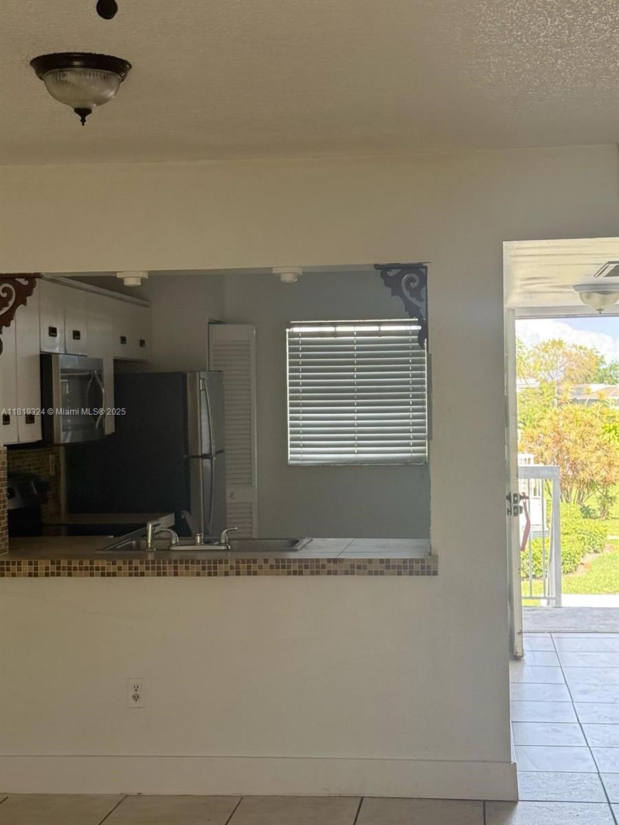 A kitchen with a pass-through window overlooks a living area with an adjacent exterior door — 438 NE 210th Cir Ter # 4B, Miami FL 33179, MIAMI, FL