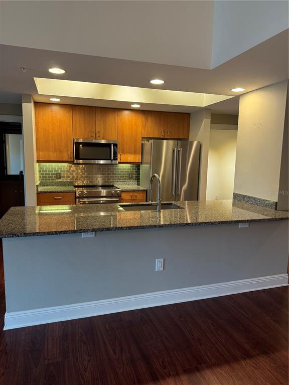 A kitchen with wood cabinets, stainless steel appliances, and a granite-topped breakfast bar — 800 N TAMIAMI TRAIL UNIT 211, SARASOTA, FL
