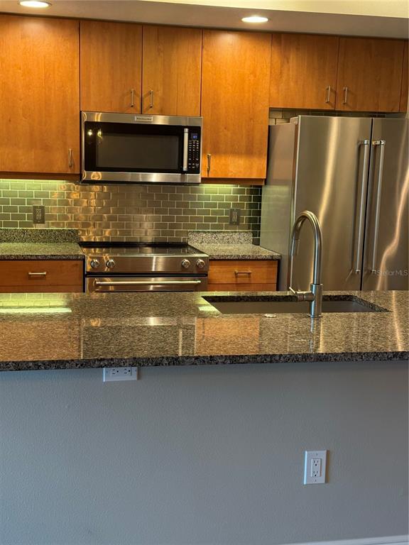 A kitchen features wood cabinets, stainless steel appliances, a granite countertop, and a tiled backsplash — 800 N TAMIAMI TRAIL UNIT 211, SARASOTA, FL