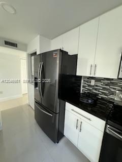 A modern kitchen features white cabinets, black countertops, a tiled backsplash, and a stainless refrigerator — MIAMI, FL