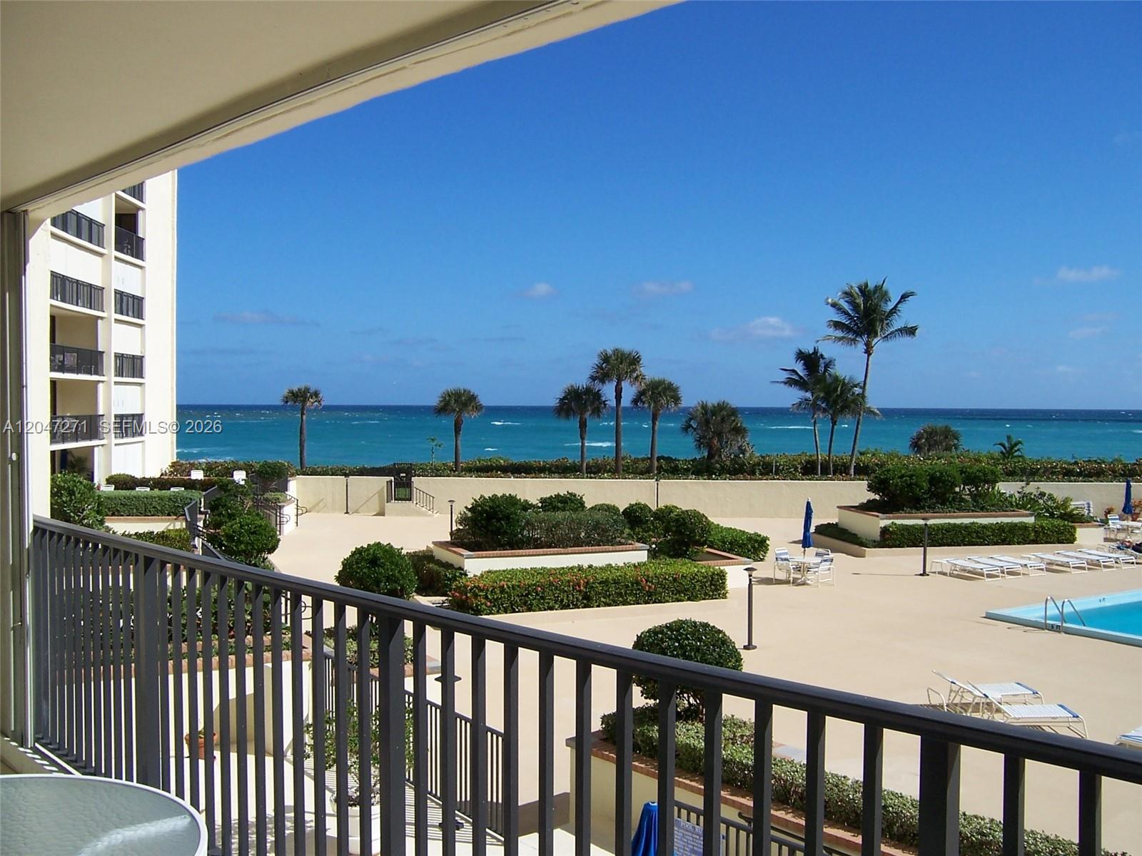 A balcony view overlooks a pool deck, landscaped gardens, and the ocean — JUPITER, FL