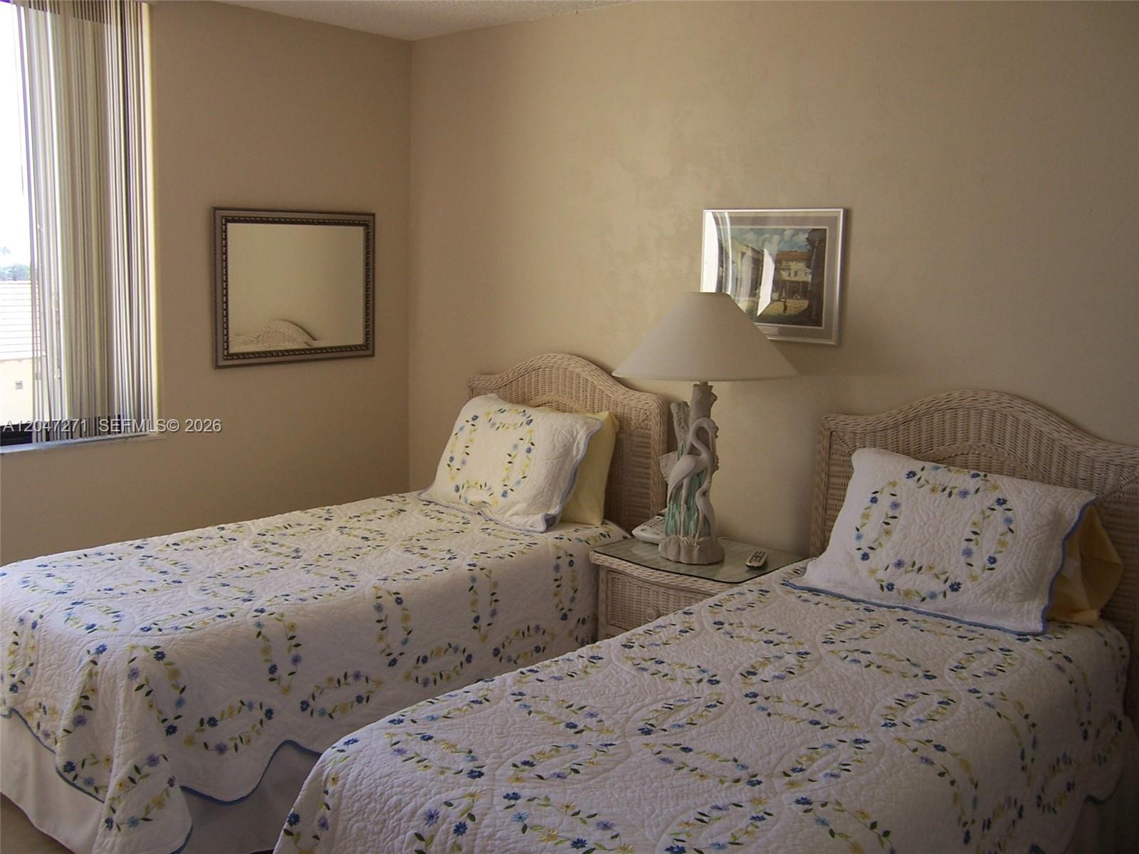A bedroom features two twin beds with floral quilts, a nightstand, and a table lamp — JUPITER, FL