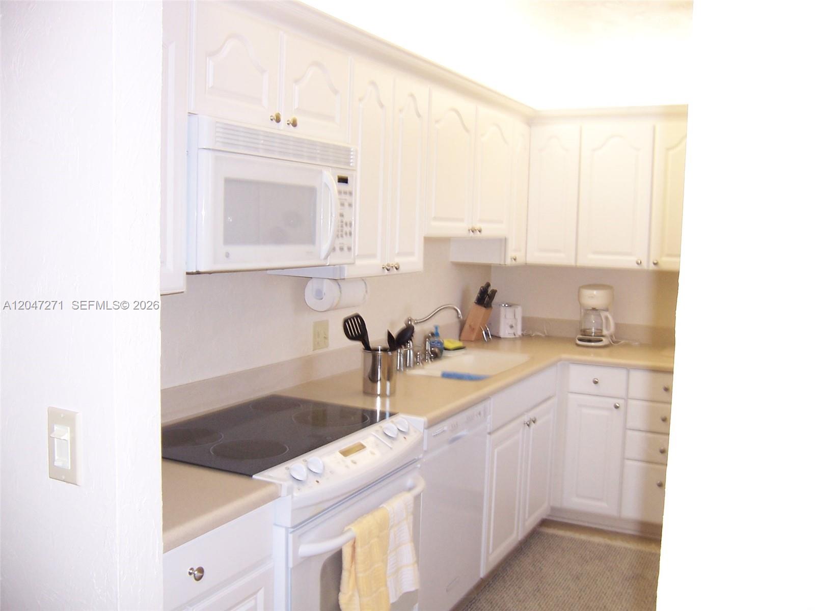 A kitchen features white cabinetry, a glass-top stove, a microwave, and light-colored countertops — JUPITER, FL