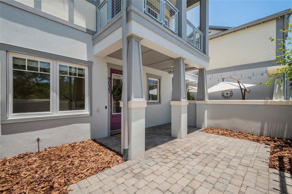 A paved patio leads to a covered entryway with a purple door and gray columns — 9037 LAUREATE BOULEVARD, ORLANDO, FL