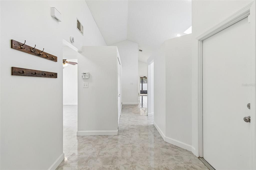 A bright hallway with white walls, vaulted ceilings, tiled floors, and two wall-mounted coat racks — 243 RAPSCALLION COURT, ORLANDO, FL