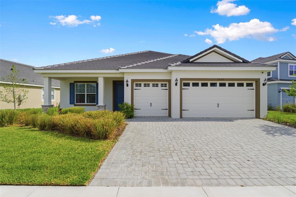 A single-story house with a two-car garage and a paved driveway under a blue sky — 2592 WISE RIVER LANE, ZEPHYRHILLS, FL